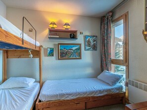 A room with bunk beds, a shelf with books, framed artwork, and a window with a view.