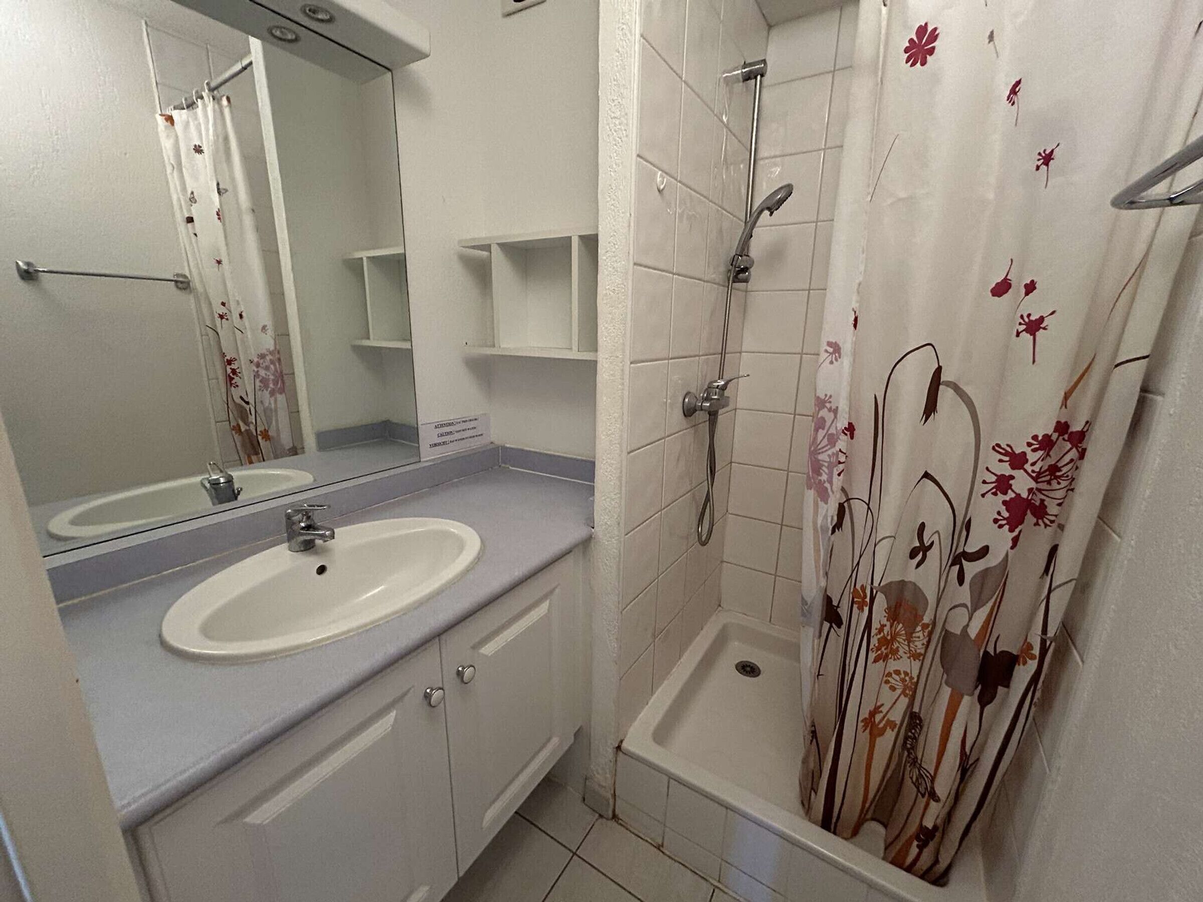 Un baño con lavamanos, espejo, ducha y cortina de ducha con motivos florales.