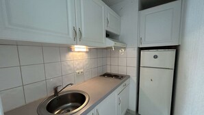 Eine kleine Küche mit weißen Schränken, einer Edelstahl-Spüle und einem weißen Kühlschrank.