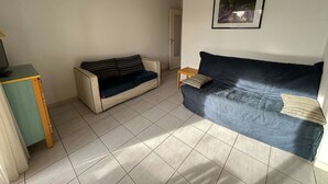 Ein Wohnzimmer mit einem beigefarbenen Sofa, einem dunkelblauen Sofa, einem kleinen Holztisch und einem gerahmten Bild an der Wand.