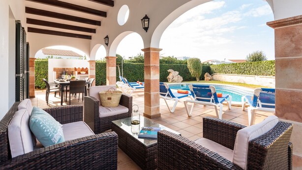Eine Außenpatio-Terrasse mit Korbmöbeln, einem Pool und einer Essgruppe.