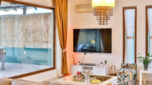 A modern living room with a sofa, a coffee table, a TV, and a decorative chandelier. - Villa Fiore (Antalya)