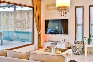 A modern living room with a sofa, a coffee table, a TV, and a decorative chandelier. - Villa Fiore (Antalya)
