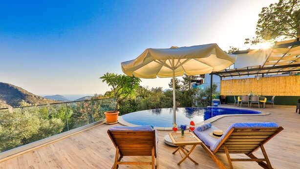 A wooden deck with a pool, lounge chairs, and a table with an umbrella. - Villa Fiore (Antalya)