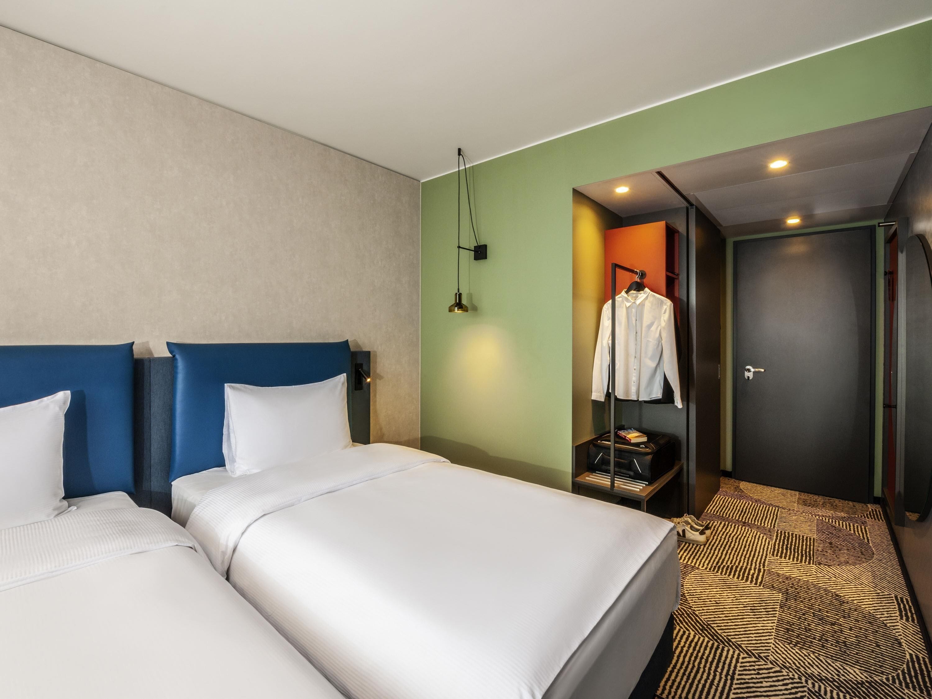 A hotel room with two beds, a wardrobe, a hanging garment, and a door leading to another room.
