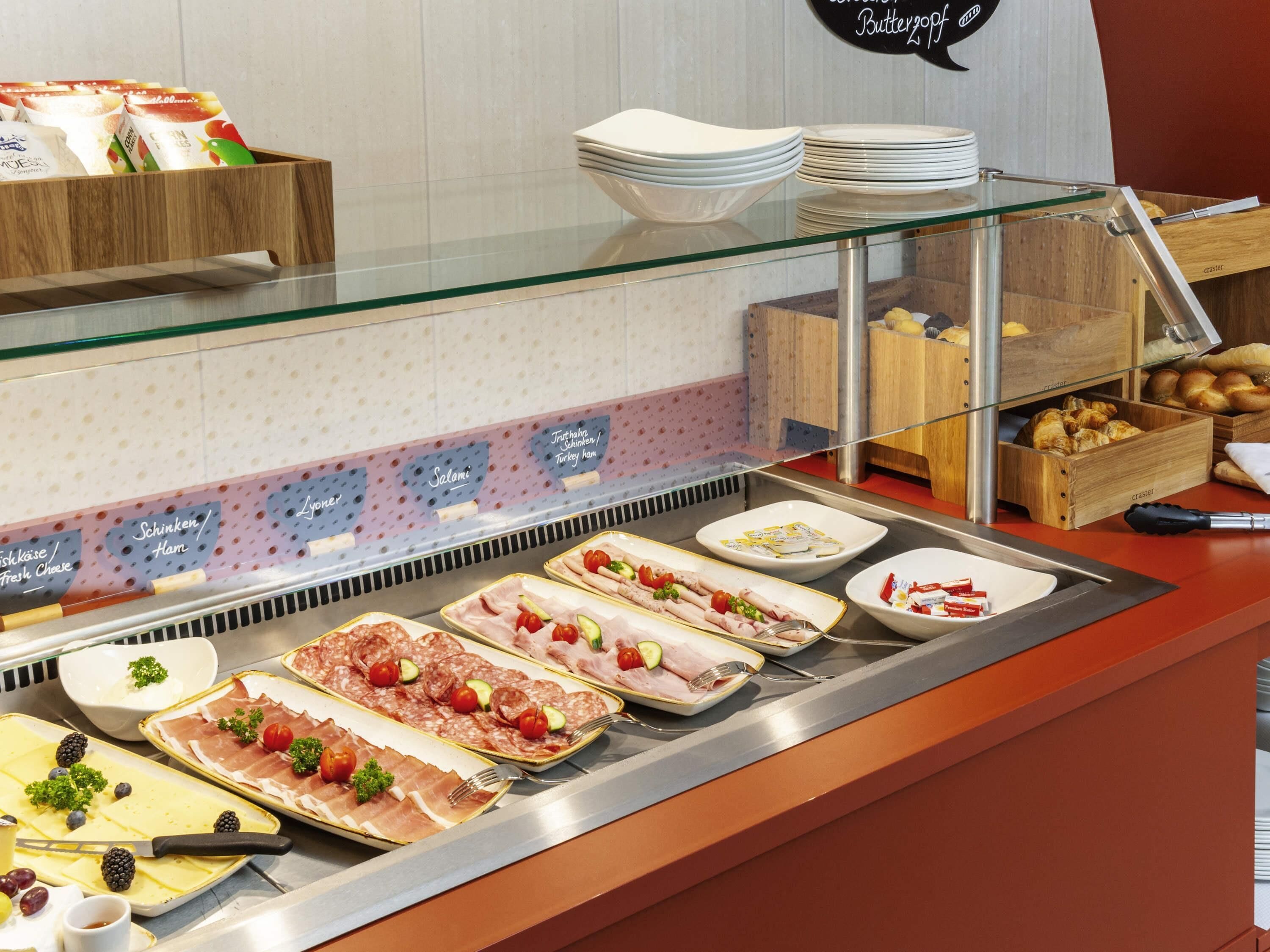A buffet with various food items, including meats and cheeses, and a glass display case.
