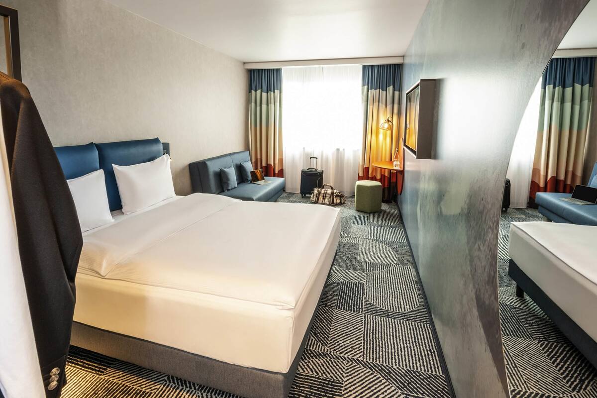 Une chambre d’hôtel avec un grand lit, un canapé, un bureau avec une lampe et une valise.