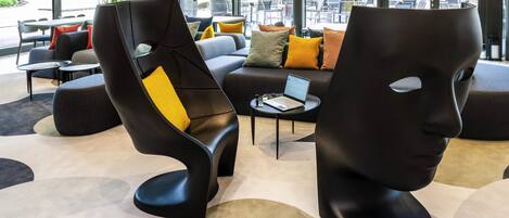 A modern lounge area with black and yellow chairs, a sofa, and a laptop on a small table.