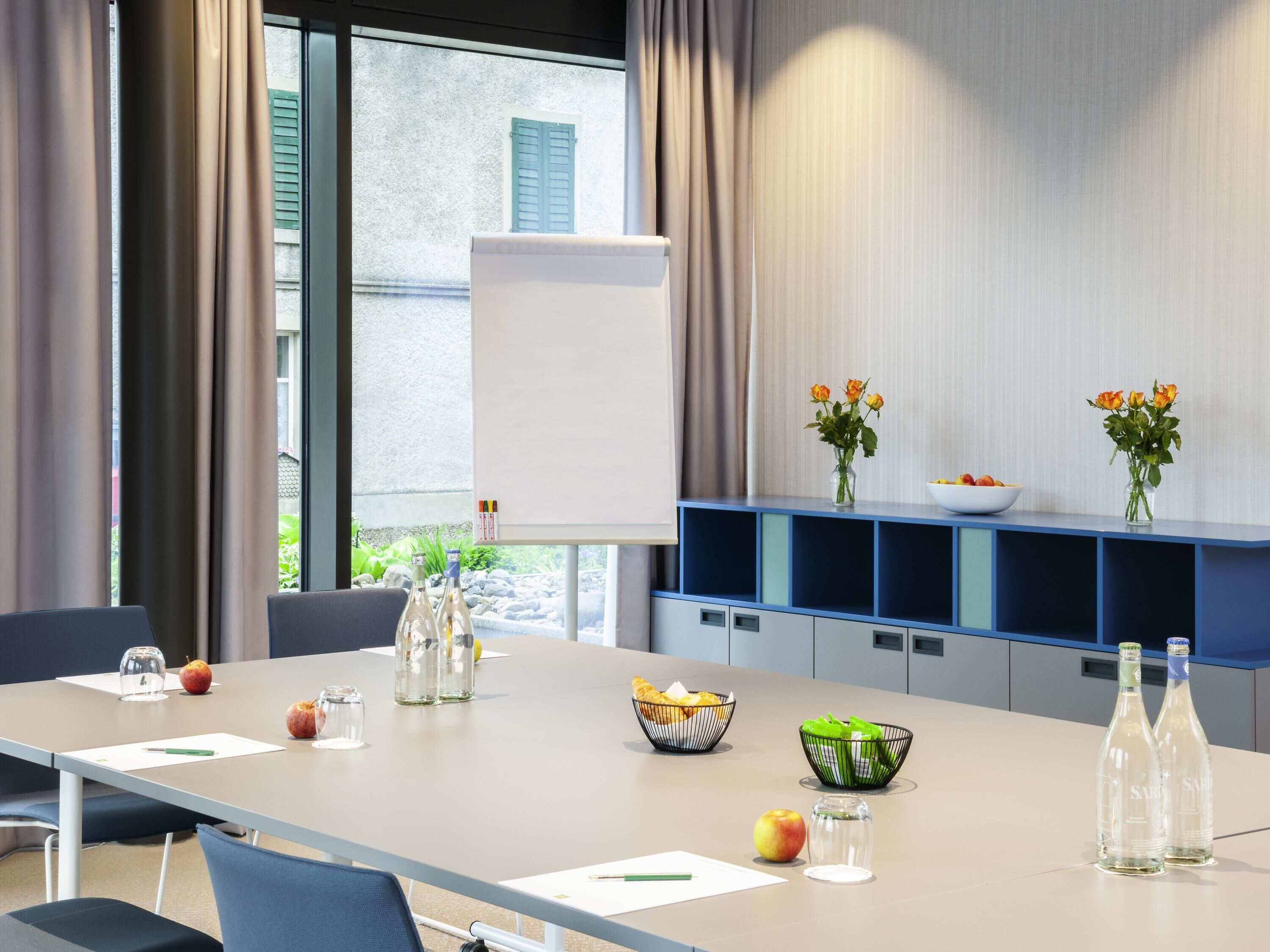 A conference room with a long table, chairs, a whiteboard, and a blue shelving unit with vases and bowls.