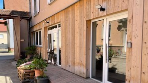 A building with wooden exterior walls, large glass doors, and a brick-paved entrance area with potted plants. - Charming cottage in the countryside near Strasbourg (Fessenheim-le-Bas)