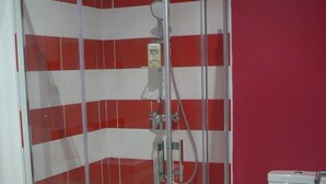 Une salle de bain avec une douche à parois de verre, des toilettes blanches et un mur recouvert de carreaux rouges et blancs.