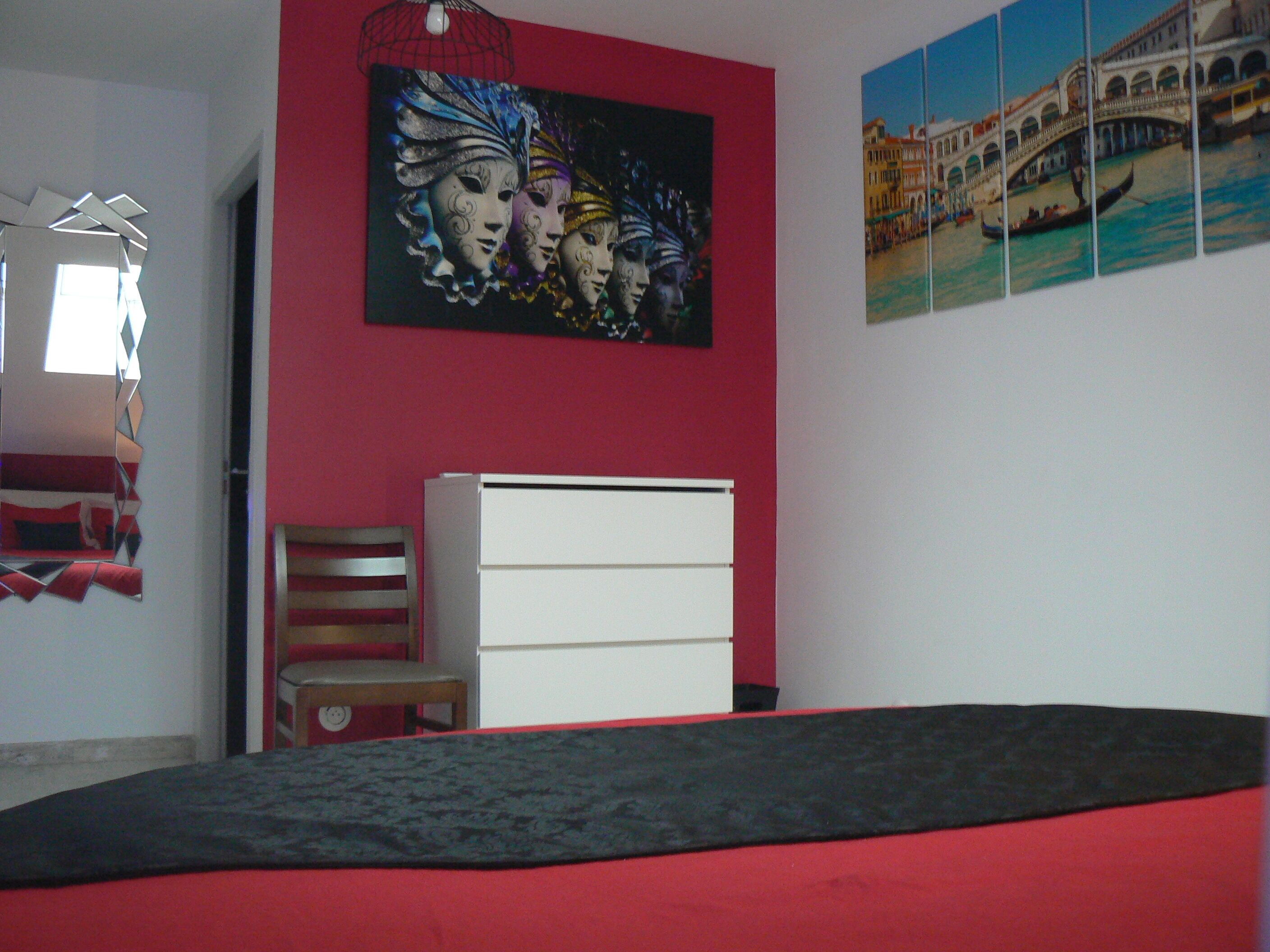 Ein Schlafzimmer mit roter Wand, einem Bett, einer weißen Kommode und einem Stuhl.