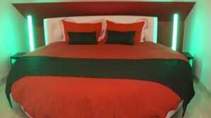 Un grand lit avec une couvre-lit rouge et noire, deux oreillers et une tête de lit en bois dotée d’un éclairage vert.