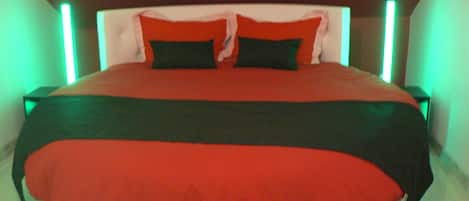 A large bed with a red and black bedspread, two pillows, and a wooden headboard with green lighting.