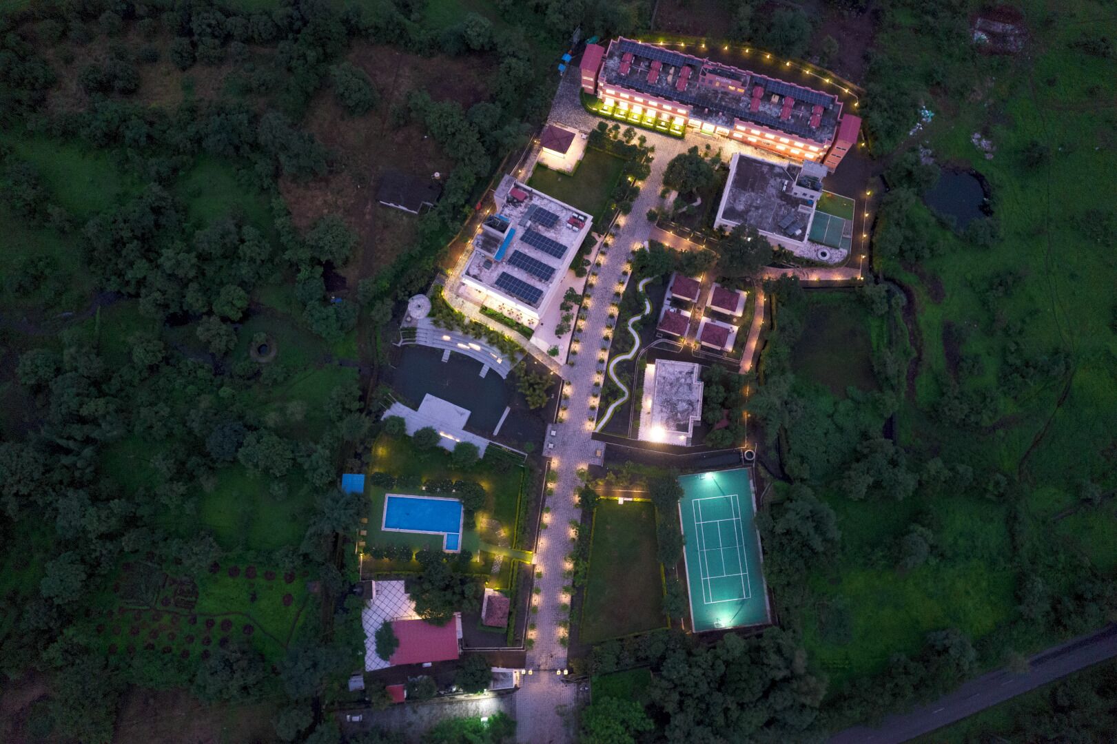 Vista aérea de un complejo con varias construcciones, incluyendo una estructura central grande con techo rojo, varias edificaciones más pequeñas y una cancha de tenis.