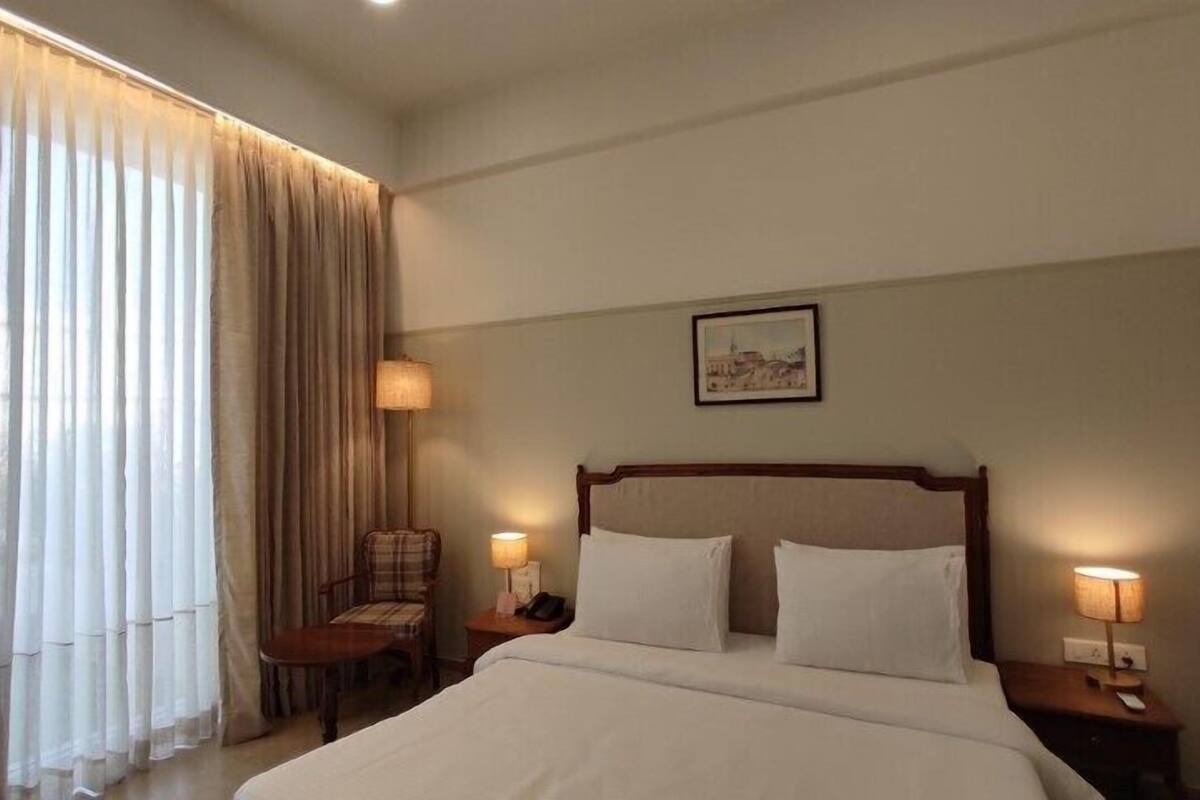 A hotel room with a large bed, two bedside tables with lamps, a chair, and a window with curtains.