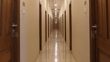 Un largo y estrecho pasillo de hotel con puertas de madera a ambos lados, suelo de baldosas y una serie de luces a lo largo del techo.