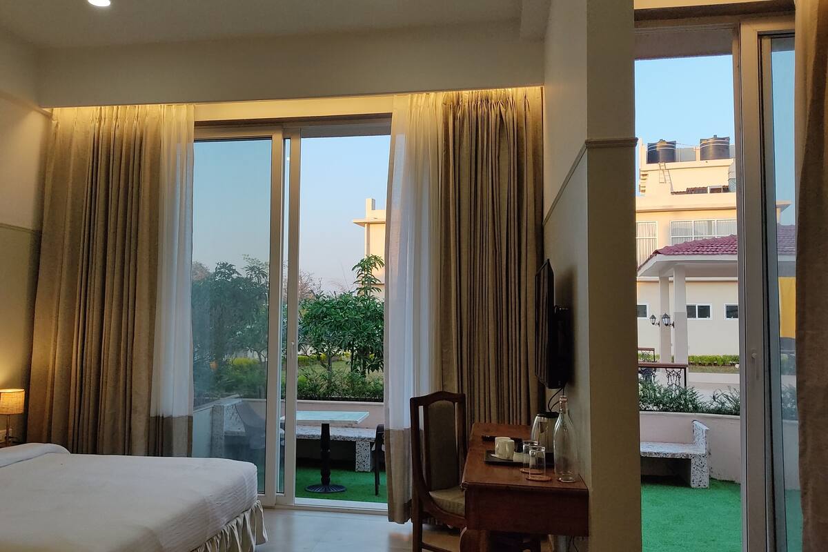 A hotel room with a bed, a desk with a chair, and a view of the outdoors through large glass doors.