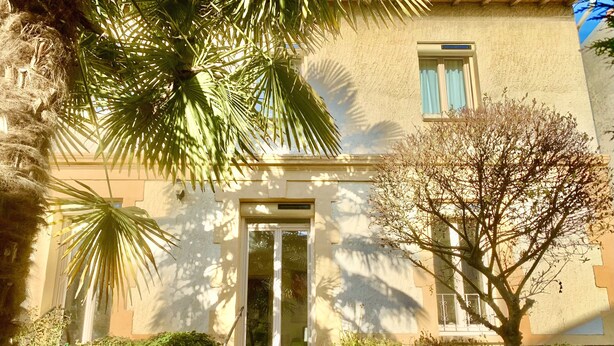 Un bâtiment doté d’une façade en pierre, d’une entrée centrale avec des marches et d’une fenêtre ornée de volets bleus.