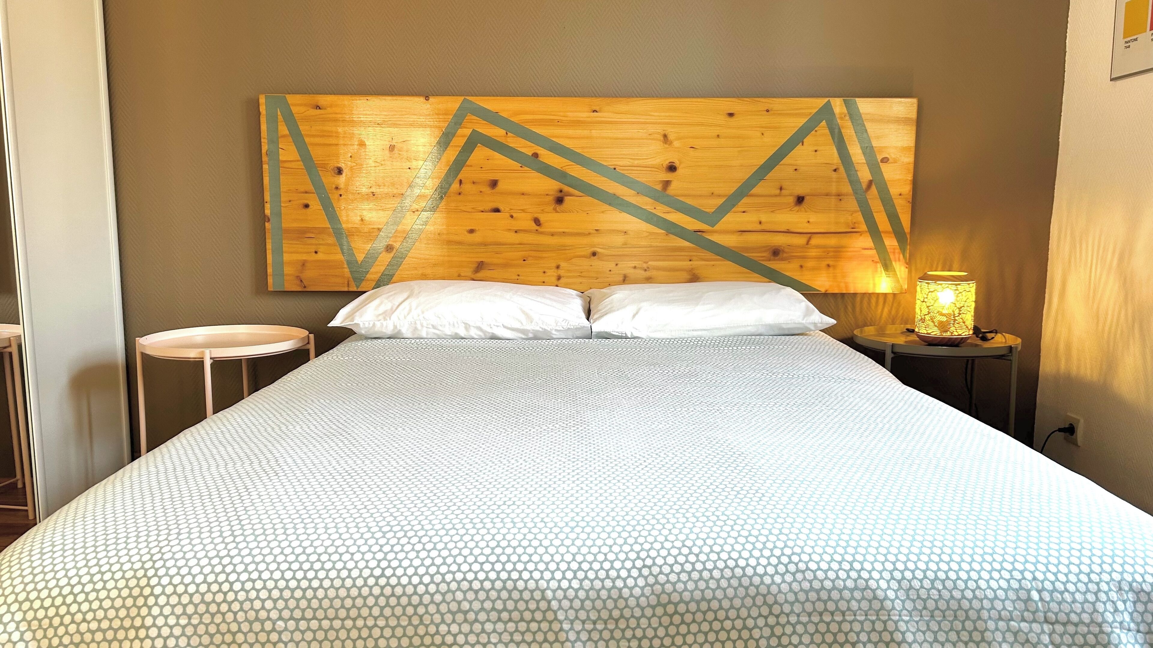 Une chambre d’hôtel avec un grand lit, deux tables de chevet, une œuvre d’art accrochée au mur et une petite table de nuit avec une lampe.