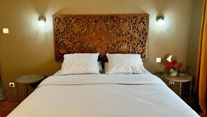 Une chambre d’hôtel avec un grand lit, deux tables de chevet, une tête de lit décorative et une petite table sur laquelle est posé un vase de fleurs.