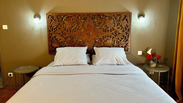 Habitación de hotel con una cama grande, dos mesitas de noche, un cabecero decorativo y una pequeña mesa con un florero.
