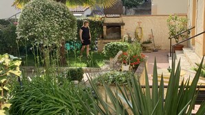 Un jardin où l’on trouve une grande variété de plantes, ainsi qu’un espace patio aménagé avec une table et des chaises.