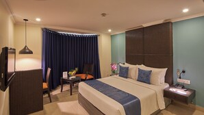 A hotel room with a large bed, a desk with a chair, a TV, and a nightstand with a lamp.