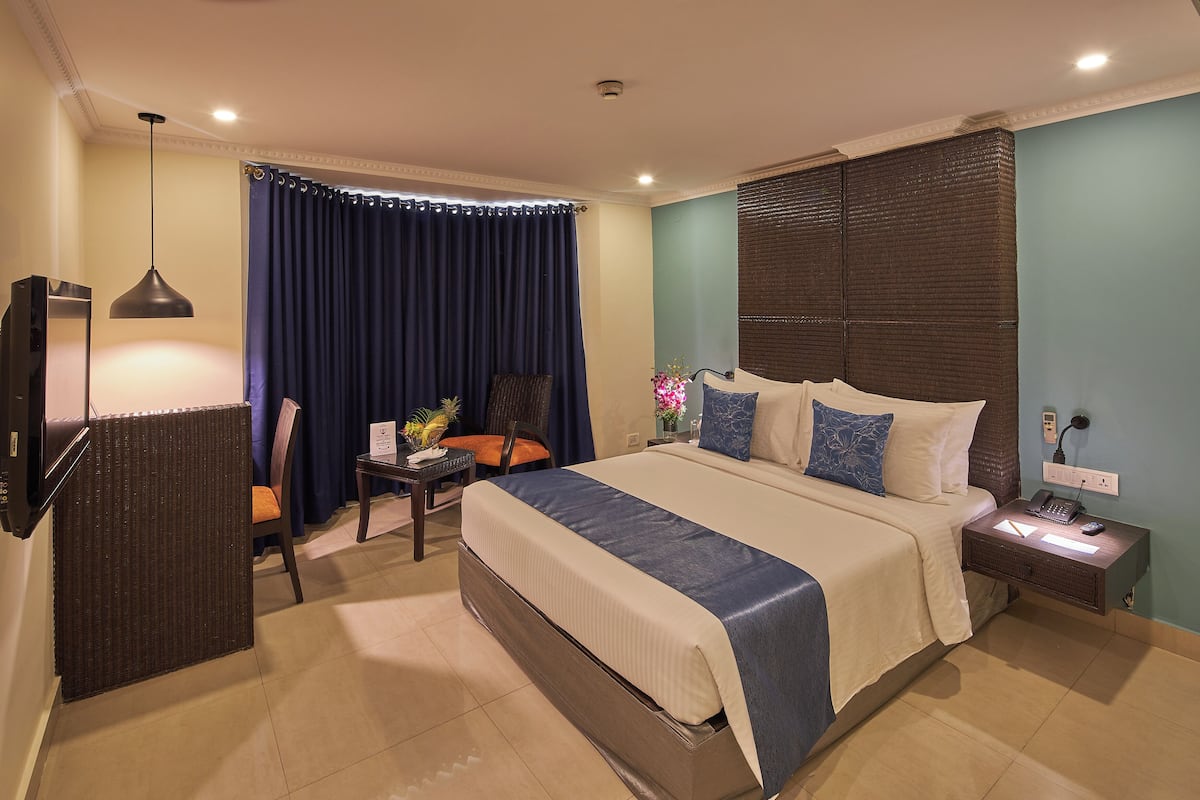 A hotel room with a large bed, a desk with a chair, a TV, and a nightstand with a lamp.