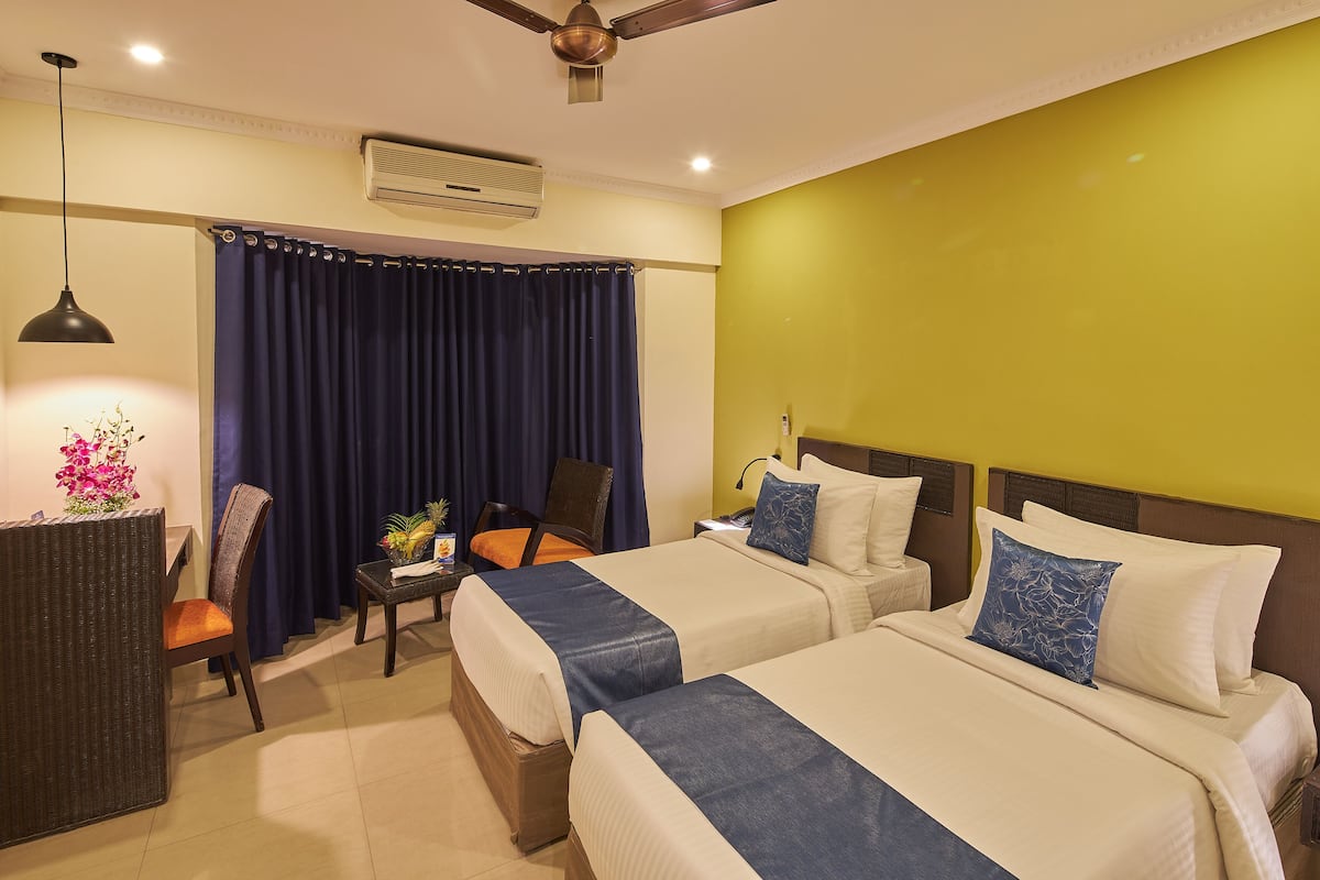 A hotel room with two beds, a desk, a chair, and a ceiling fan.