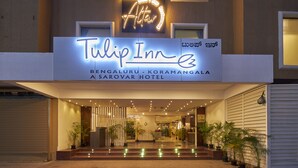 The exterior of Tulip Inn, Bengaluru - Koramangala Hotel with a neon sign, entrance, and potted plants.