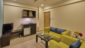 A living room with a sofa, a coffee table, a television, a kitchen area, and a ceiling fan.