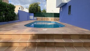 Una piscina con borde de piedra y escalones de acceso, rodeada por un muro azul y otro de piedra.