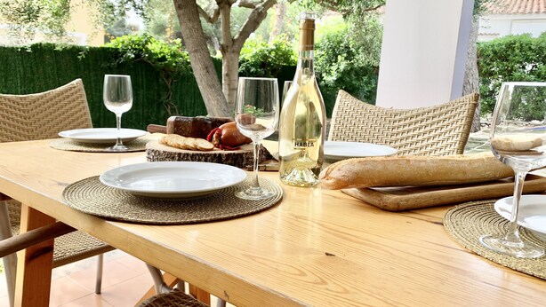Una mesa de madera servida con platos, copas, una botella de vino, pan y una tabla de madera con pan y queso rebanados.
