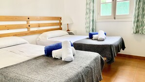 Habitación de hotel con dos camas, cabecera de madera, mesita de noche con lámpara y ventana con cortinas.