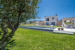 Un edificio moderno de dos pisos con piscina, mobiliario exterior y una pérgola.