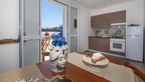 A modern kitchen with wooden cabinets, a white refrigerator, and a dining area with a table set for two. - Sicily luxury Marzamemi (Noto)