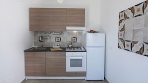A compact kitchen with wooden cabinets, a white refrigerator, a gas stove, and a hanging light fixture. - Sicily luxury Marzamemi (Noto)