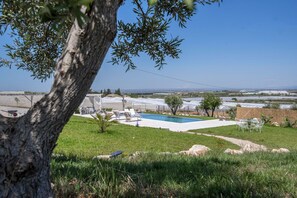 Zona de piscina con sillas de descanso, una pérgola y vistas a campos de cultivo.