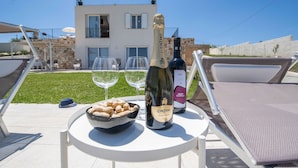 A table with a bottle of Cinzano wine, two glasses, and a bowl of peanuts on a sunny patio with a modern house in the background. - Sicily luxury Marzamemi (Noto)