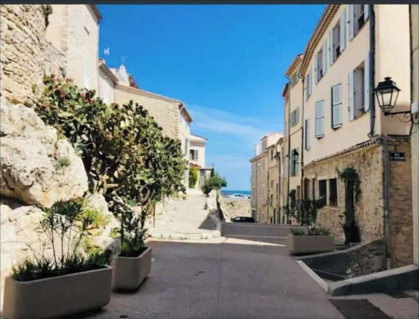 Un vicolo stretto con edifici in pietra, piante in vaso e un cielo azzurro limpido.