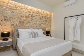 A bedroom with a stone wall, a bed with white bedding, two bedside lamps, and a robe rack with white robes.