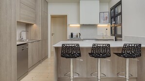 A modern kitchen with wooden cabinets, a built-in dishwasher, a central island with bar stools, and a framed picture on the wall. - THIRAMENOUS RESIDENCE - SIX BEDROOM HOUSE with Rooftop Hot Tub (Athina)