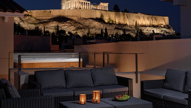 A rooftop terrace with wicker furniture, a bar, and a view of the Acropolis at night. - THIRAMENOUS RESIDENCE - SIX BEDROOM HOUSE with Rooftop Hot Tub (Athina)