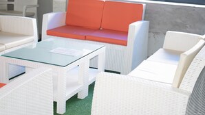 A seating area with white wicker furniture, including a sofa and chairs, and a glass-top table. - Emmy Hotels and Suites (Lekki)