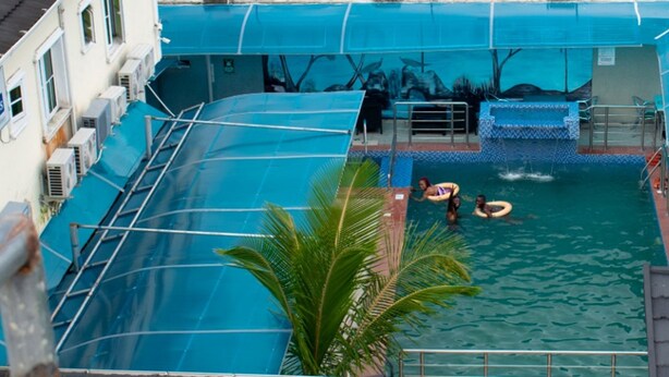 A swimming pool with a blue cover, a palm tree, and a lifeguard stand. - Emmy Hotels and Suites (Lekki)