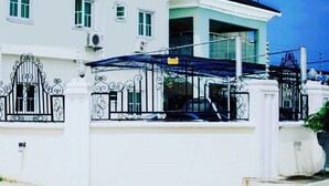 A white two-story house with a black roof, a gated entrance, and a covered carport. - Emmy Hotels and Suites (Lekki)