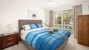 A bedroom with a large bed, a wooden nightstand, a bedside table, a lamp, a framed picture on the wall, and a window with curtains. - Clifden Cottage in Cowes (Cowes)