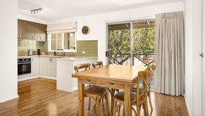 A modern kitchen with wooden cabinets, a built-in oven, and a dining area with a wooden table and chairs. - Clifden Cottage in Cowes (Cowes)