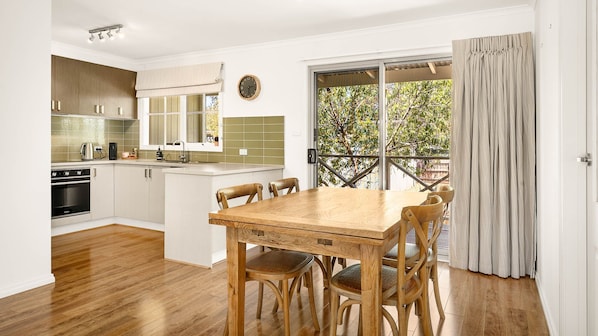 A modern kitchen with wooden cabinets, a built-in oven, and a dining area with a wooden table and chairs.